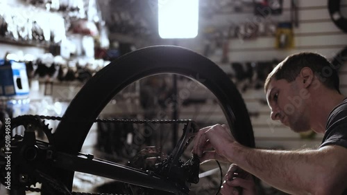 Bicycle wheel repair. man works in workshop. Caucasian master of service turns wheel and checks tension of chain. bicycle repair small businesses.  service center for the repair of sports equipment
