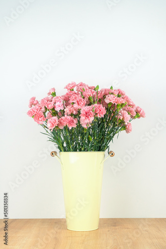 Fototapeta Naklejka Na Ścianę i Meble -  Close-up of a lot of pink carnations in a tin vase with handles on a wooden table on a neutral background. Vertical photo