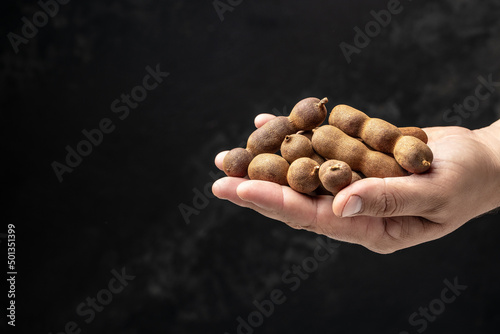 male hands holding Tamarinds set beans in shell on a brown butchers block on a dark background, Tropical healthy fruits. banner, menu, recipe place for text