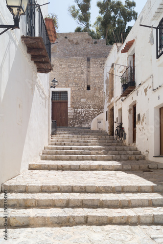 Narrow street in the old town of Ibiza known as Dalt Vila. Black bicycle in an empty street in the old city. Stairs in a stone pedestrian street with old houses with white painted walls. © Alejandro Tapia