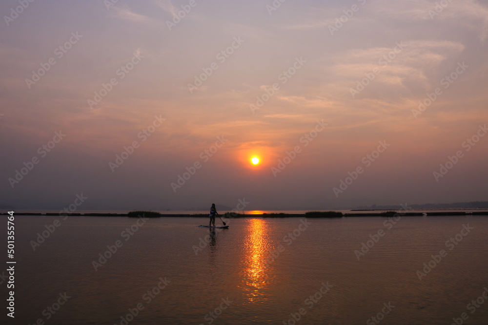 Asian woman playing surfboard in the river in the morning with beautiful sunrise.