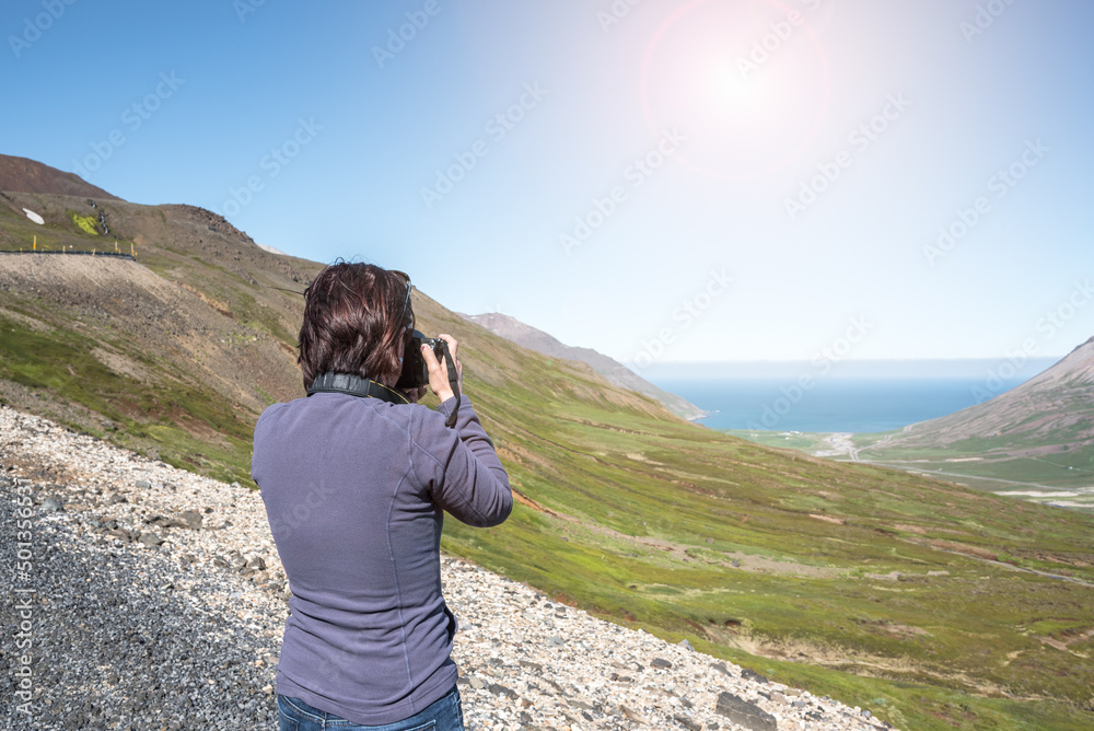 Woman photographer taking pictures of a valley from a mountain pass in Iceland on a sunny summer day