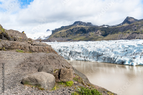 Majestic glacier in Iceland on a partly cloudy summer day. Hikers admiring the glacier are visible on the left hand side of the pictures.
