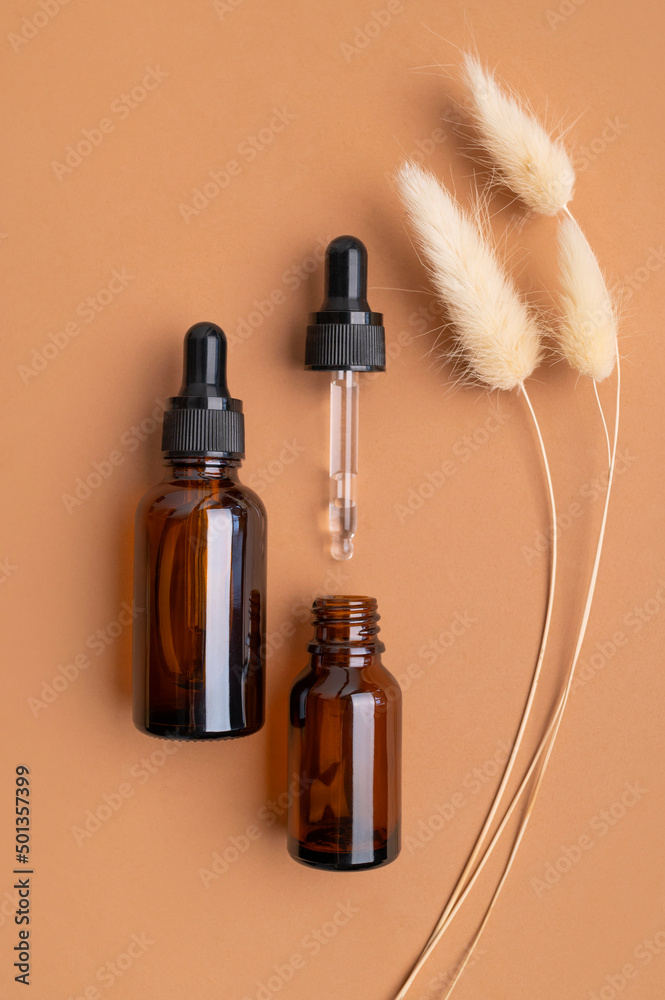 Clean brown glass cosmetic bottles with pipette, jar of cream, decorative spikelets plants on brown background. Natural organic cosmetics. Spa products for health and beauty. Serum, facial oil