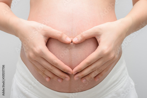 Pregnant woman making hand gesture a heart shape on her belly.