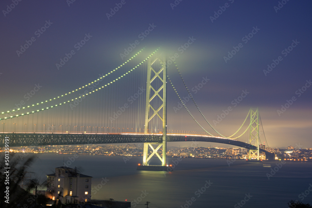 Traffic moves along suspension bridge lit up on cloudy night