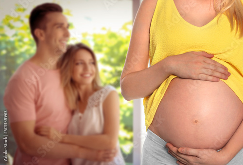 Surrogacy concept. Young pregnant woman and blurred view of happy couple indoors photo