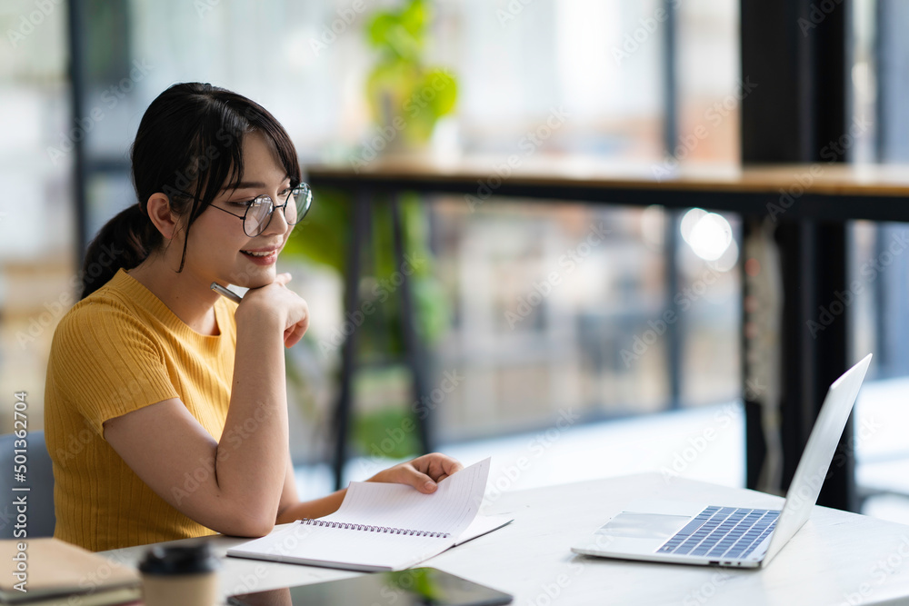 Fototapeta premium Portrait of Asian businesswoman with laptop writes on a document at her office