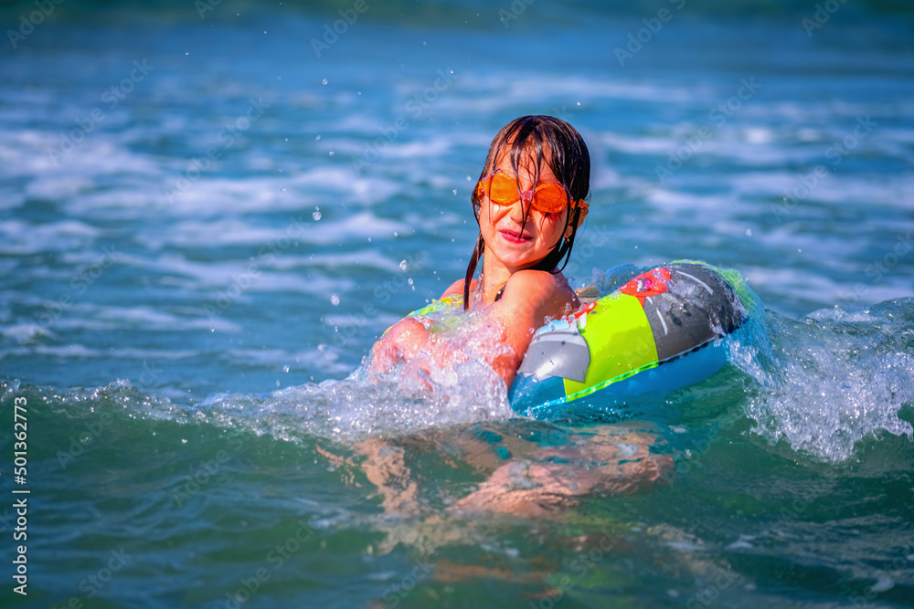 Portrait of hppy child girl swimming on the waves of sea. Summer vacation and healthy lifestyle concept.
