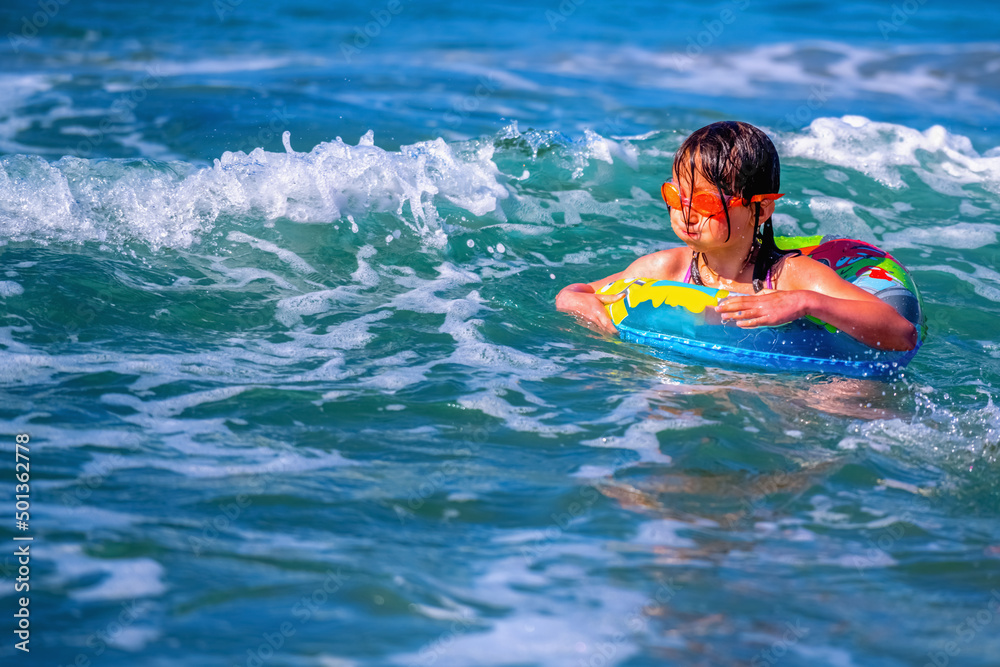 Portrait of hppy child girl swimming on the waves of sea. Summer vacation and healthy lifestyle concept. Copy space. Horizontal image.