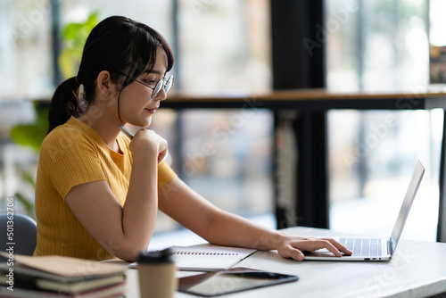 Charming Asian woman working on a laptop and tablet at the office. Looking at the laptop. online learning and video conferencing Free Download Charming Asian woman working on a laptop and tablet at the office. Looking at the laptop. online learning and video conferencing - GFXLoad