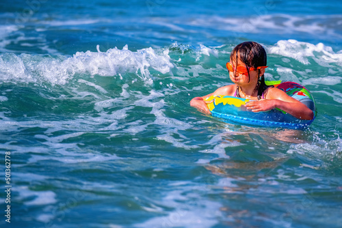 Portrait of hppy child girl swimming on the waves of sea. Summer vacation and healthy lifestyle concept. Copy space. Horizontal image.