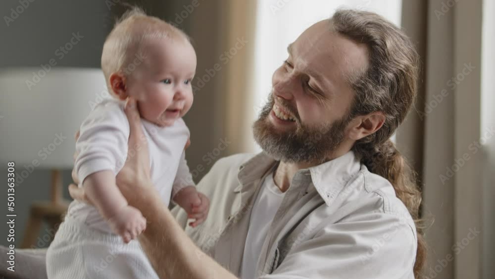 Close-up happy father loving caring middle-aged dad bearded man holding little daughter son child jumping laughing male parent spend time together at home with baby parenting infant newborn alone Close-up happy father loving caring middle-aged dad bearded man holding little daughter son child jumping laughing male parent spend time together at home with baby parenting infant newborn alone