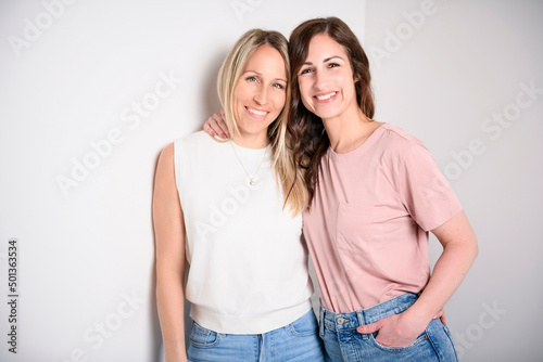 Two smiling best girl friends blond and brunette on white background. Closeup face portrait of two young beautiful women.