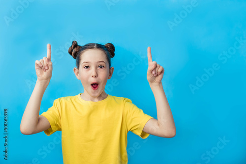 cheerful beautiful girl in a yellow T-shirt on a blue background points up her fingers