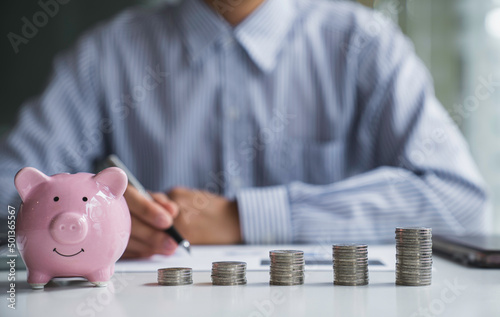 Businessman with a coin in a piggy bank along with pressing the calculator and writing down savings for the future after retirement, ideas for saving money for the future and life after retirement