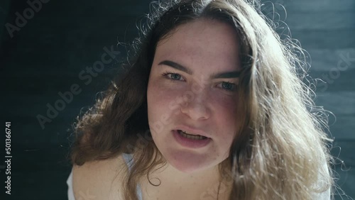 Angry overweight caucasian girl looks right into the camera and screams with a grimace of annoyance. Close-up of hateful girl with a chubby face.