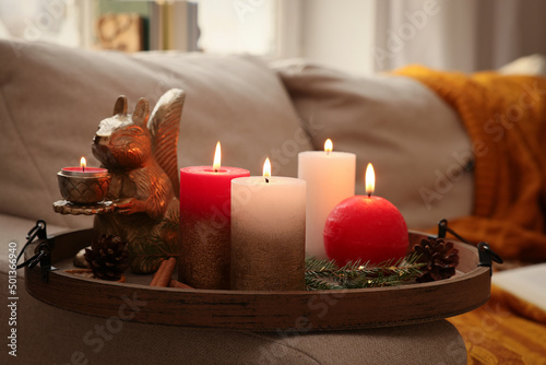 Tray with beautiful burning candles and Christmas decor on sofa at home