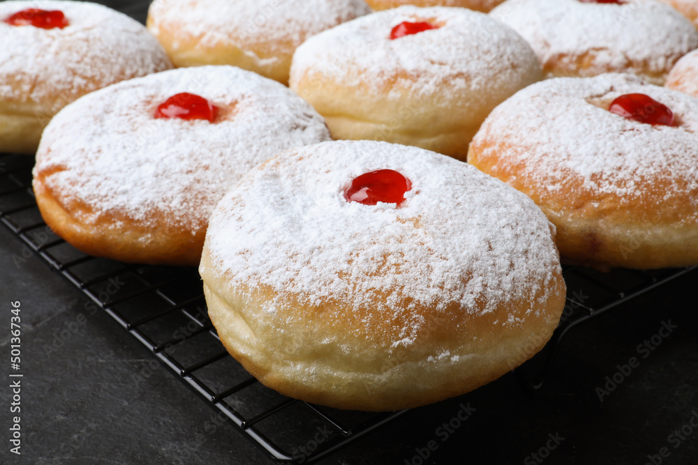 Many delicious donuts with jelly and powdered sugar on black table, closeup