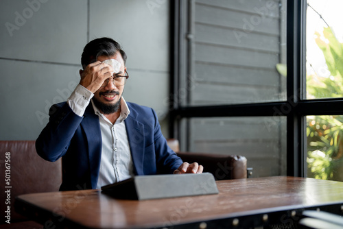 businessman looking at his laptop and is using tissue paper to wipe sweat.