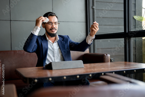 businessman looking at his laptop and is using tissue paper to wipe sweat.