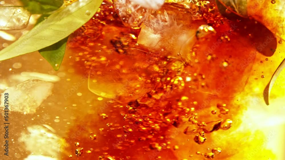 Super slow motion of pouring tea into water in twister shape. Fresh green leaves and ice cubes inside. Filmed on high speed cinema camera, 1000fps.