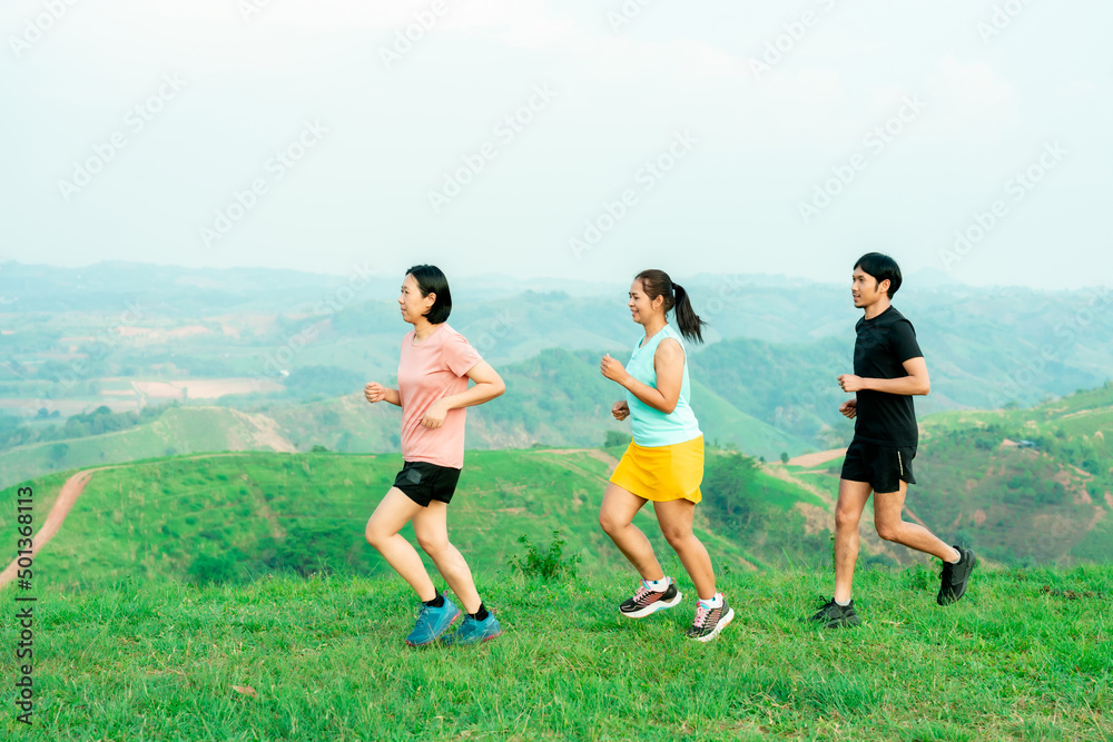 Group of friends Asian man and female trail runners. Wearing sportswear practicing on a trail running in the mountains behind a beautiful mountain on a clear day. Practice running happily Group of friends Asian man and female trail runners. Wearing sportswear practicing on a trail running in the mountains behind a beautiful mountain on a clear day. Practice running happily