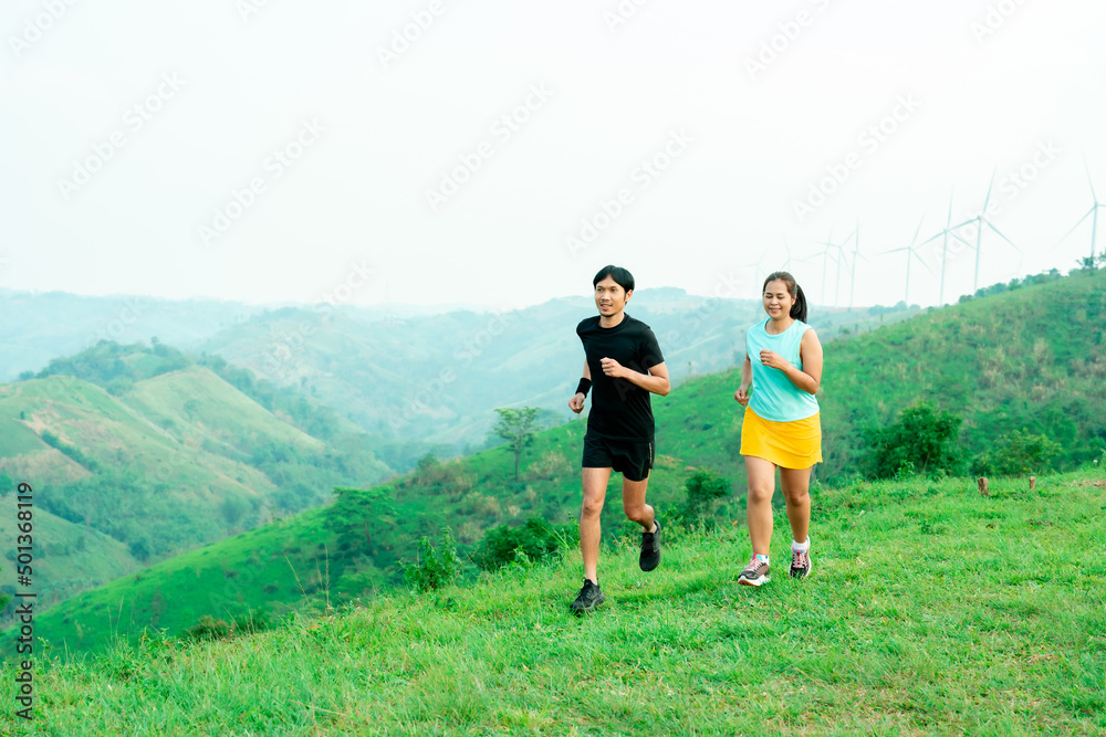couple Asian man and female trail runners. Wearing sportswear practicing on a trail running in the mountains behind a beautiful mountain on a clear day. Practice running happily couple Asian man and female trail runners. Wearing sportswear practicing on a trail running in the mountains behind a beautiful mountain on a clear day. Practice running happily