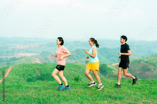 Group of friends Asian man and female trail runners. Wearing sportswear practicing on a trail running in the mountains behind a beautiful mountain on a clear day. Practice running happily
