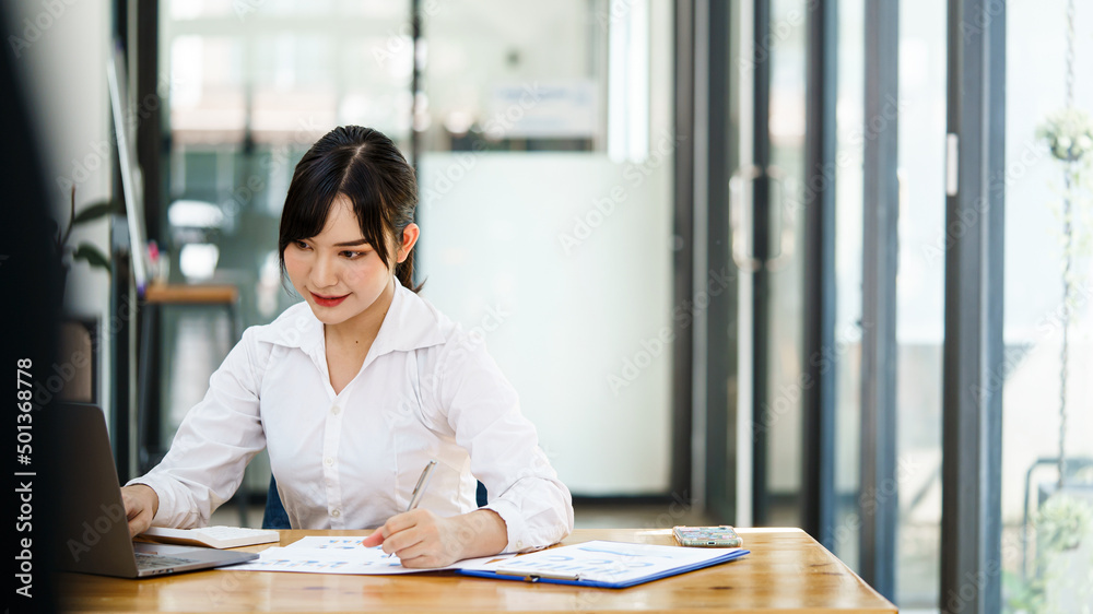 Young beautiful smile Asian businesswoman using her laptop while sitting in a chair at her working place. Young beautiful smile Asian businesswoman using her laptop while sitting in a chair at her working place.