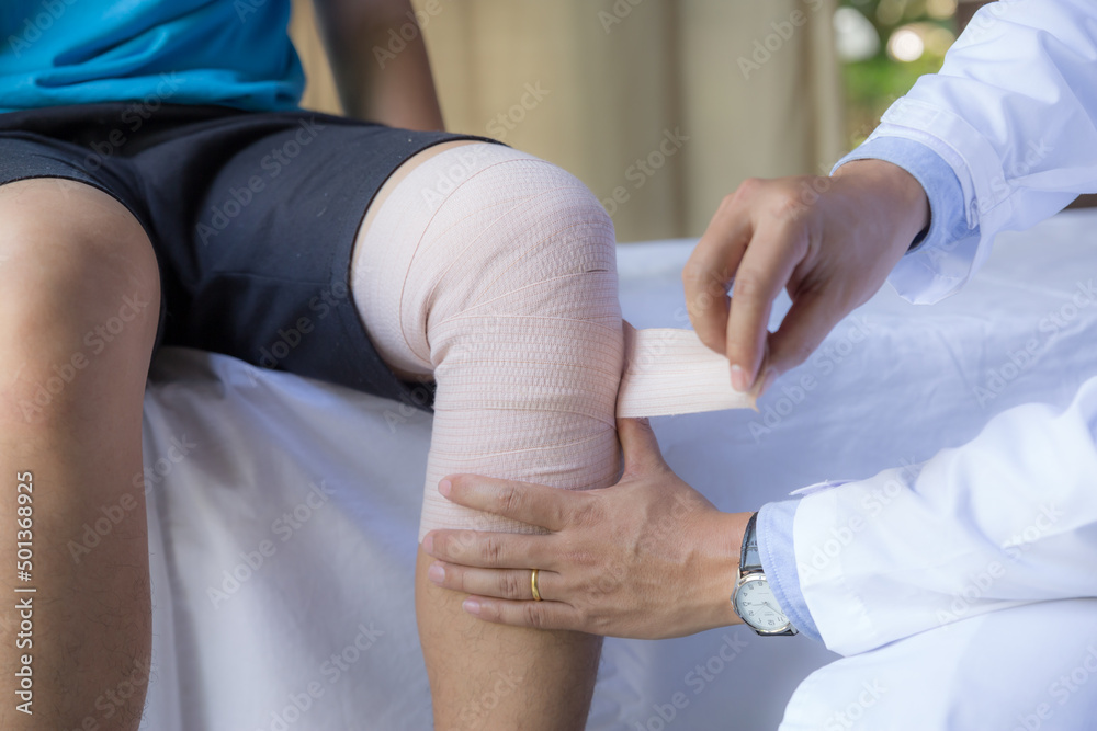 Doctor consultant puts medical bandage roll around the patient's knee. Heal injuries.