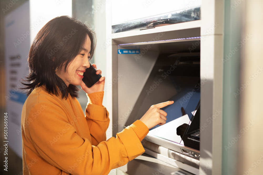 Happy smiling young woman withdrawing money from credit card. Young woman typing pin code on keypad of ATM machine. Happy smiling young woman withdrawing money from credit card. Young woman typing pin code on keypad of ATM machine.