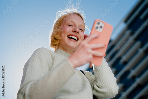 Happy girl walking on the street checking phone. Beautiful blonde girl typing a message