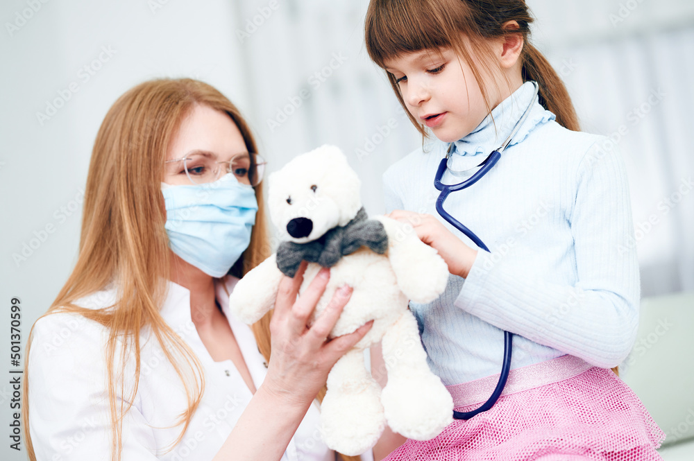 Caucasian female doctor with patient little girl examining by stethoscope bear toy in office Caucasian female doctor with patient little girl examining by stethoscope bear toy in office