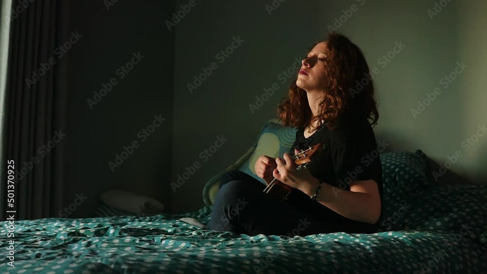 Mujer tocando el ukulele y cantando en su habitación. Concepto de musica.