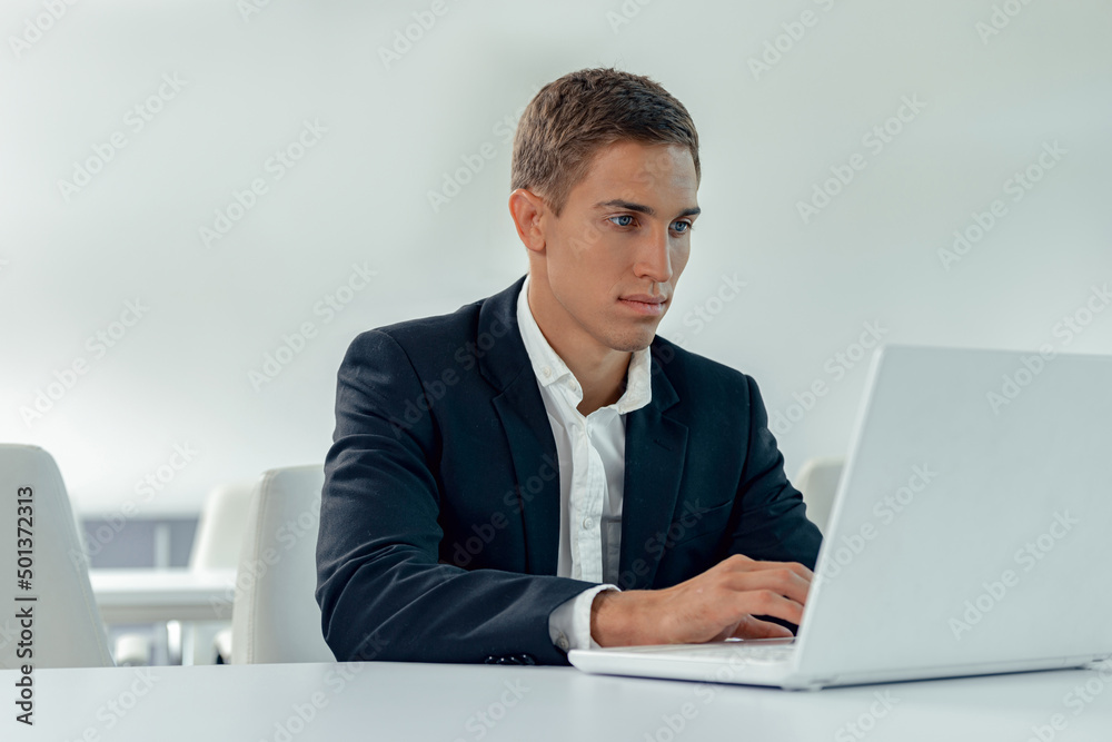 Focused man in business suit sitting in light office while working on laptop Focused man in business suit sitting in light office while working on laptop