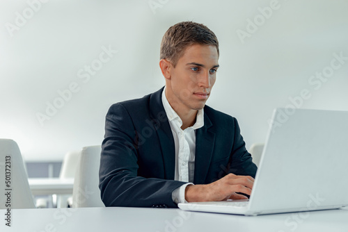 Focused man in business suit sitting in light office while working on laptop © Friends Stock
