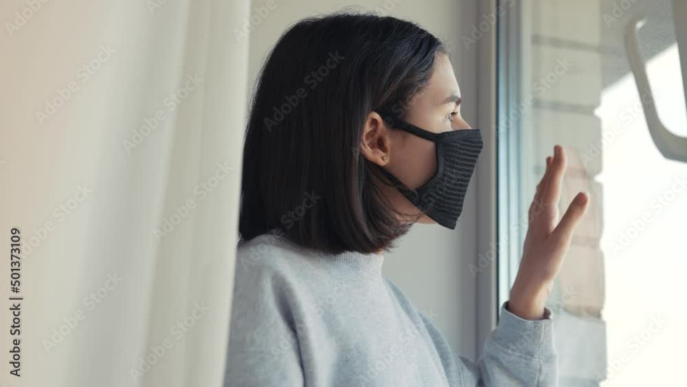 coronavirus. girl kid looks out window sad in a medical mask. stay at home. pandemic self-isolation coronavirus covid infection stay home concept. kid mask touches glass sunlight wants to go outdoor