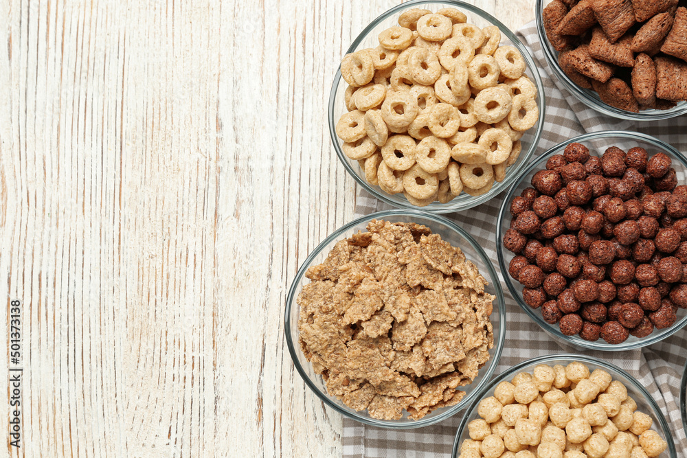 Different breakfast cereals in glass bowls on white wooden table, flat lay. Space for text Different breakfast cereals in glass bowls on white wooden table, flat lay. Space for text
