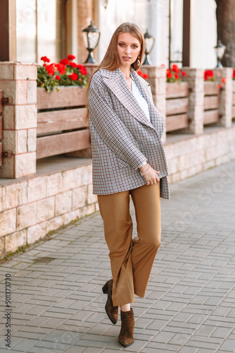 The girl is a model showing fashionable clothes on the street. Behind the girl is a cafe fence
