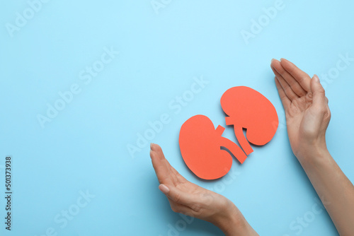 Woman protecting paper cutout of kidneys on light blue background, top view. Space for text