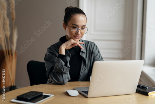 The manager is a woman with glasses working in the office using a laptop computer online project report
