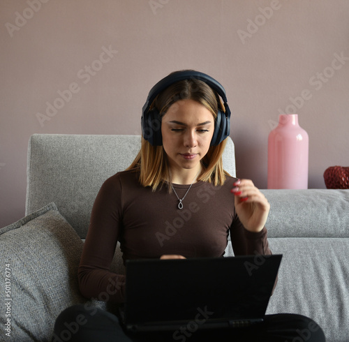 bellissima ragazza sorridente che lavora al computer con le cuffie seduta sul divano