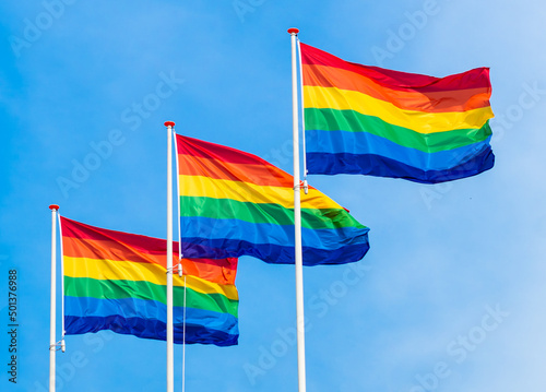 Obraz na płótnie Three LGBT Gay flags hanging and waving horizontally on blue sky background. Horizontal photo of equality symbol on Gay Pride Day in the Netherlands. w salonie
