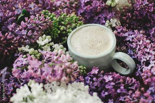 Stylish composition of lilac flowers and warm cup of coffee. Colorful lilac branches and coffee with creamy foam  good morning concept. Spring morning in countryside still life
