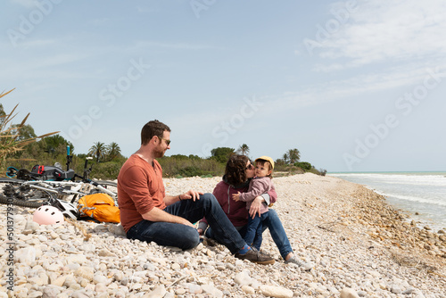 Couple and daugther sitting on a pebble beach with their bikes behind them. Sustainable transportation and healthy life. 