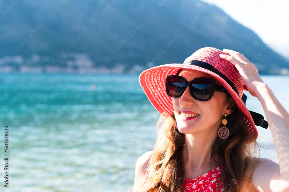 A smiling woman in red hat and red dress on the sea. Place for text. Close-up. A smiling woman in red hat and red dress on the sea. Place for text. Close-up.