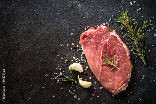 Raw meat. Fresh steak, pork steak with herbs and spices at black background. Top view with space for text.