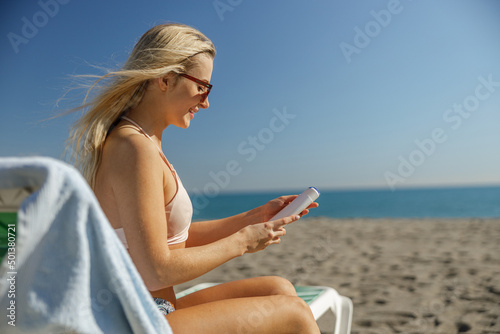 Smiling lady in sunglasses holding sunscreen body lotion while sunbathing