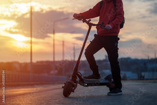 A man rides around the city on a powerful electric scooter. Road and sunset on the background